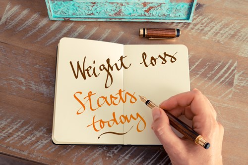 Someone writing 'Weight loss starts here' in a diary